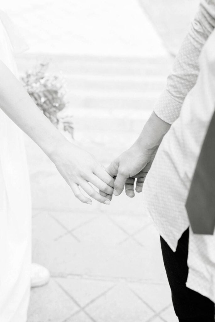 Delicate black and white photo of a couple holding hands, capturing the intimacy and elegance of a luxurious wedding moment.