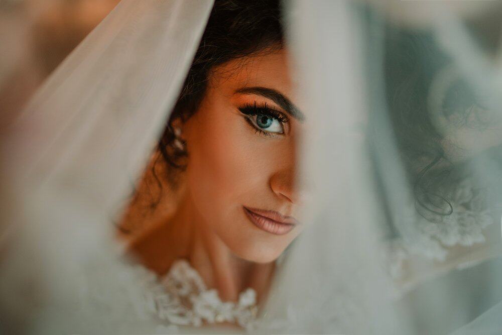 Stunning bride with blue eyes peeking through a wedding veil, highlighting elegance and beauty.
