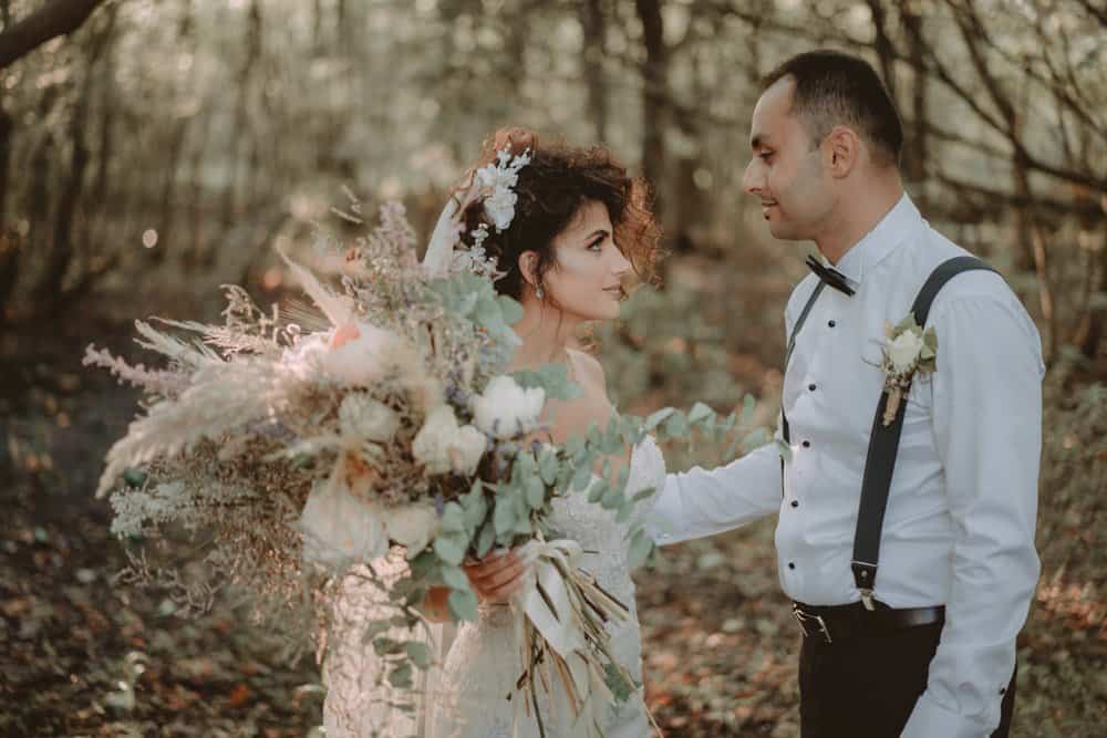 Elegant bride and groom exchanging vows in a luxurious outdoor wedding setting, surrounded by natural autumn scenery.