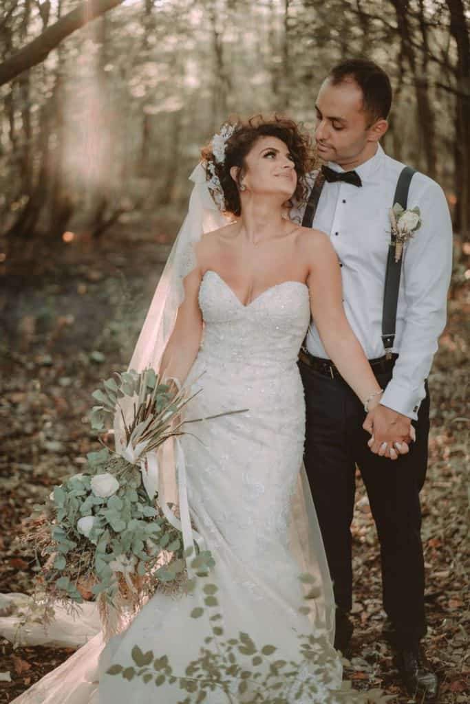 Elegant bride and groom holding hands in a forest setting, showcasing a luxury wedding scene with romantic and natural elements.