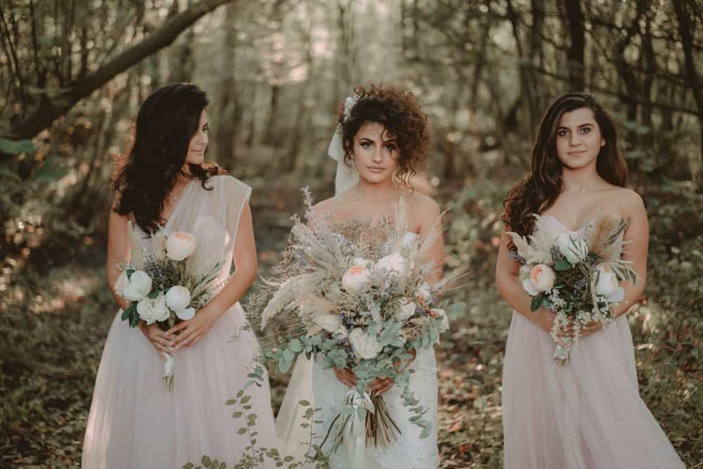 Elegant bridal trio in a forest setting with luxurious wedding bouquets, ideal for high-end wedding venues.