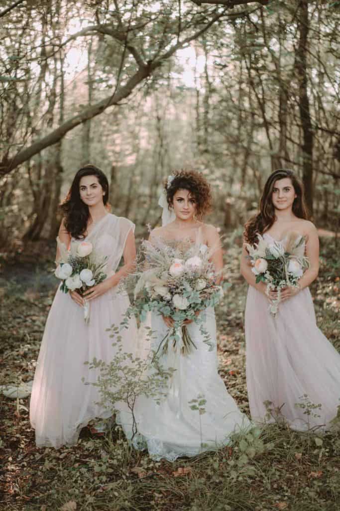 Elegant bridal portrait of three brides in a lush forest, showcasing luxury wedding attire and beautiful floral arrangements in a high-end outdoor wedding setting.