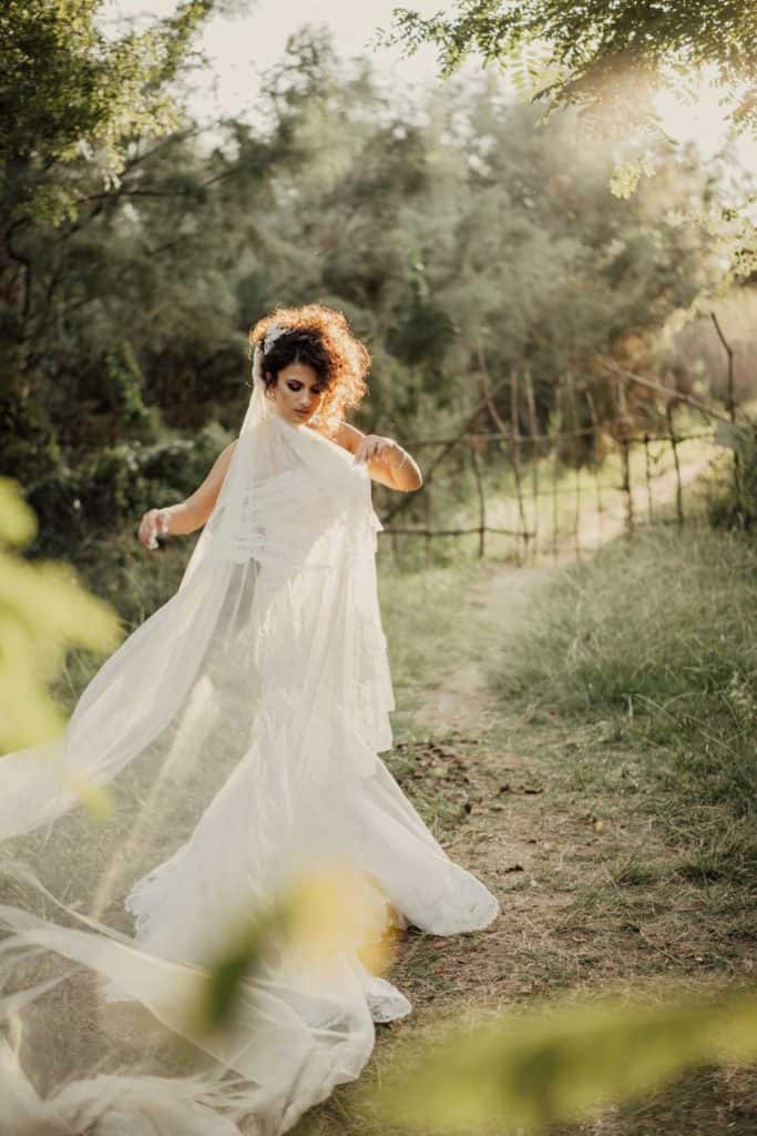 Elegant bride in a flowing white wedding gown walking through a lush garden at sunset, capturing a romantic outdoor wedding scene.