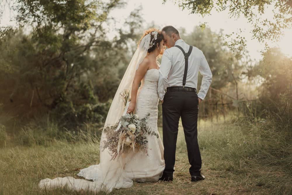 Classic outdoor wedding ceremony with bride and groom in a lush natural setting, capturing a romantic moment at sunset.