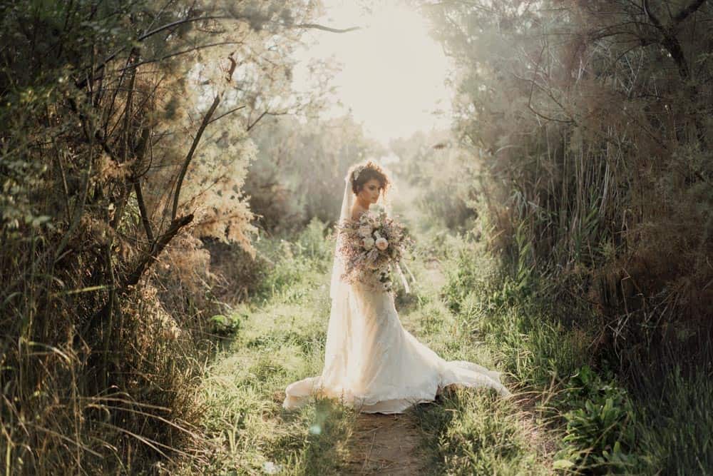 Elegant bride standing in lush greenery during a luxury outdoor wedding photoshoot.