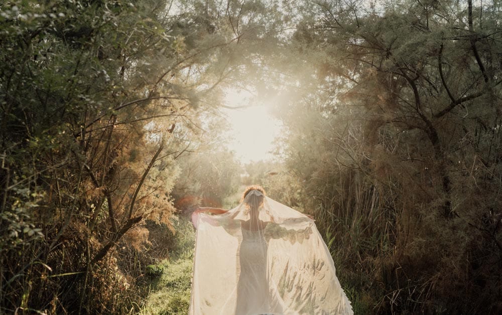 Bride in a flowing wedding dress walking through a romantic forest pathway at sunset, showcasing an elegant outdoor wedding setting.