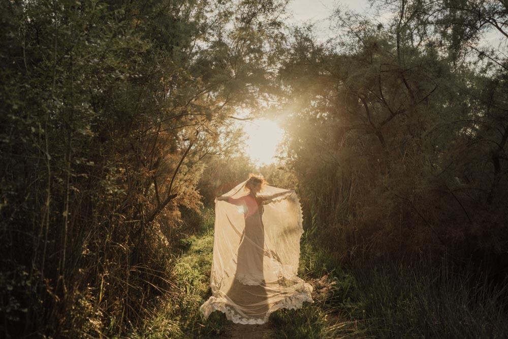 Elegant bride in flowing gown walking through lush forest at sunset, capturing natural beauty for luxury wedding photos.