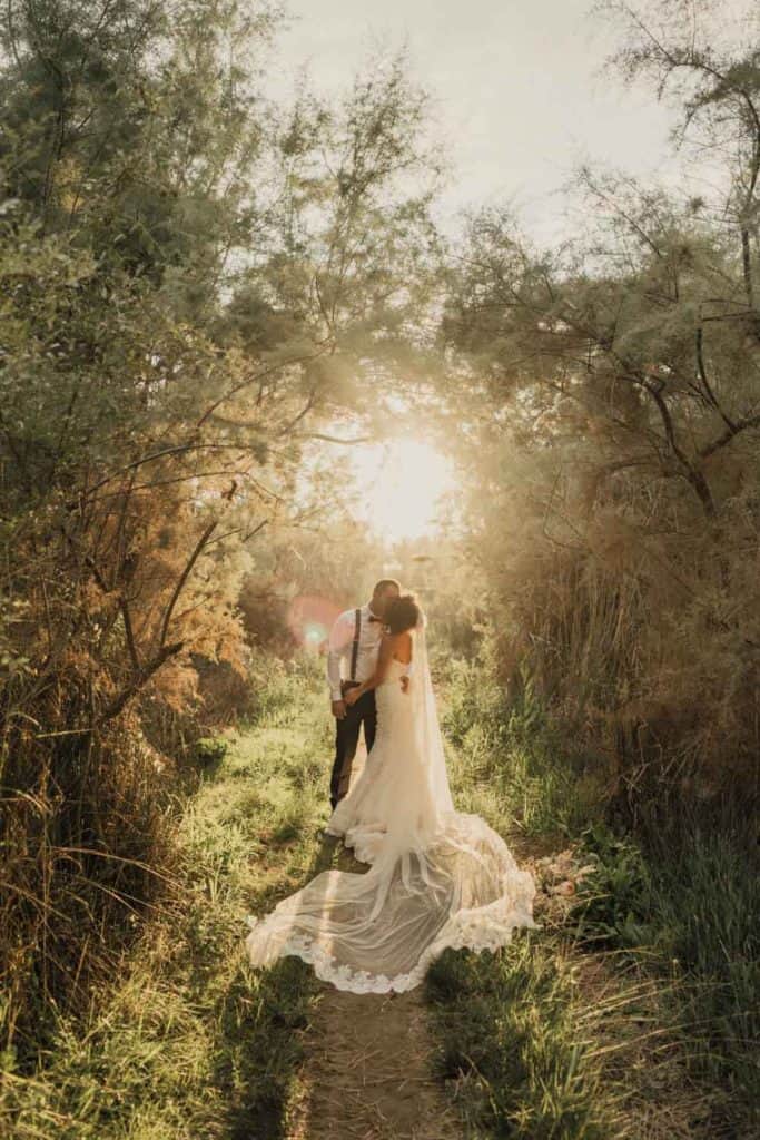 Elegant couple embrace during sunset in lush outdoor wedding setting, showcasing romantic high-end venue.