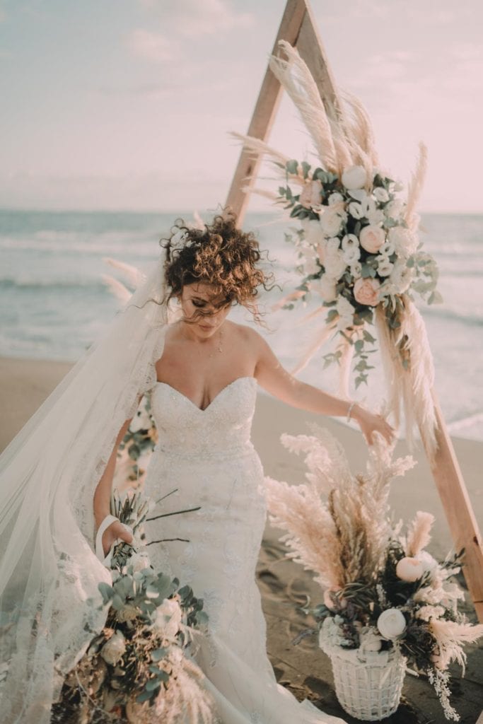 Elegant beach wedding bride in a luxurious gown with floral arrangements and a boho-chic backdrop.