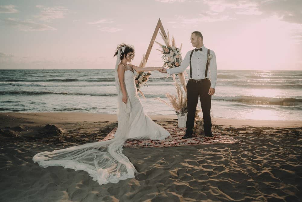 Elegant beachfront wedding ceremony with bride and groom exchanging vows at sunset.
