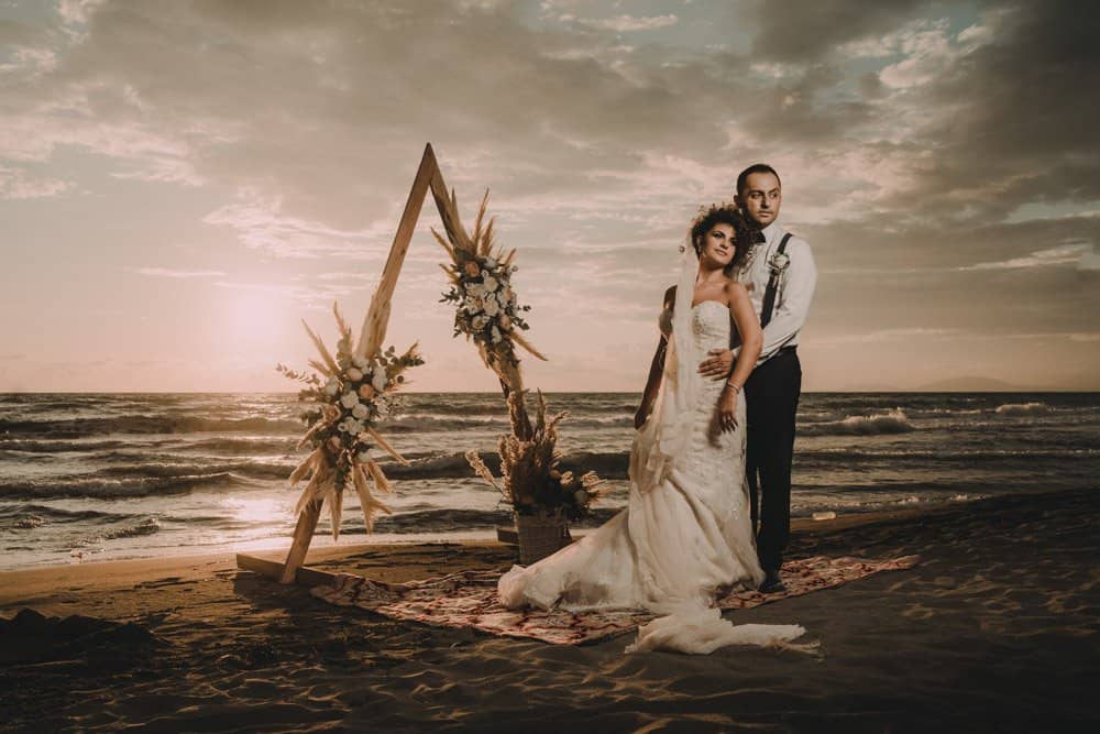 Elegant beach wedding with romantic couple and floral arch at sunset, perfect for high-end coastal wedding venues.
