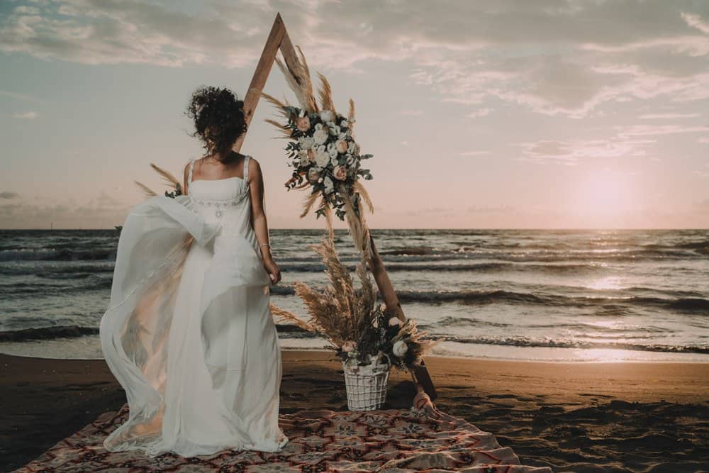 Elegant bride in a flowing white wedding gown on a luxury beach wedding set up at sunset.
