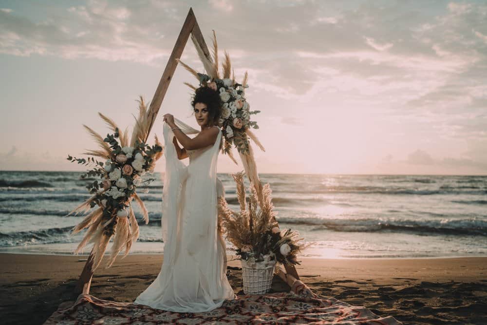 Elegant bride in a flowing wedding dress at a luxury beach wedding setup with floral arch.
