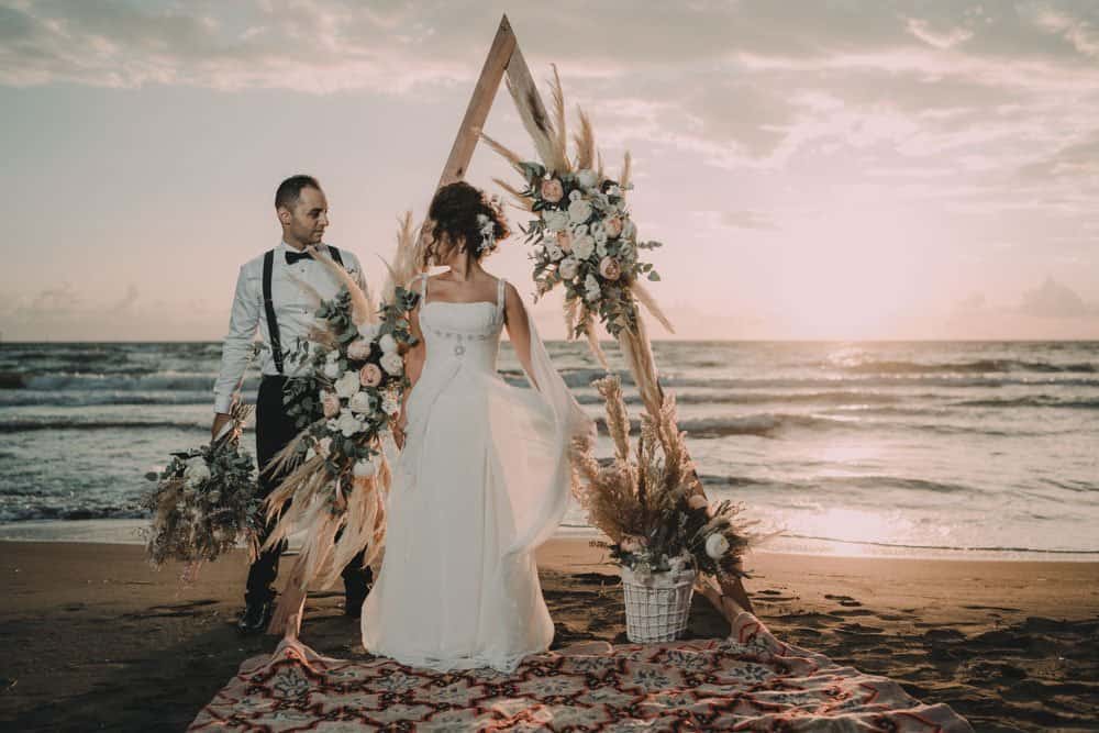 Stylish wedding ceremony on the beach with elegant floral arch and sunset view.