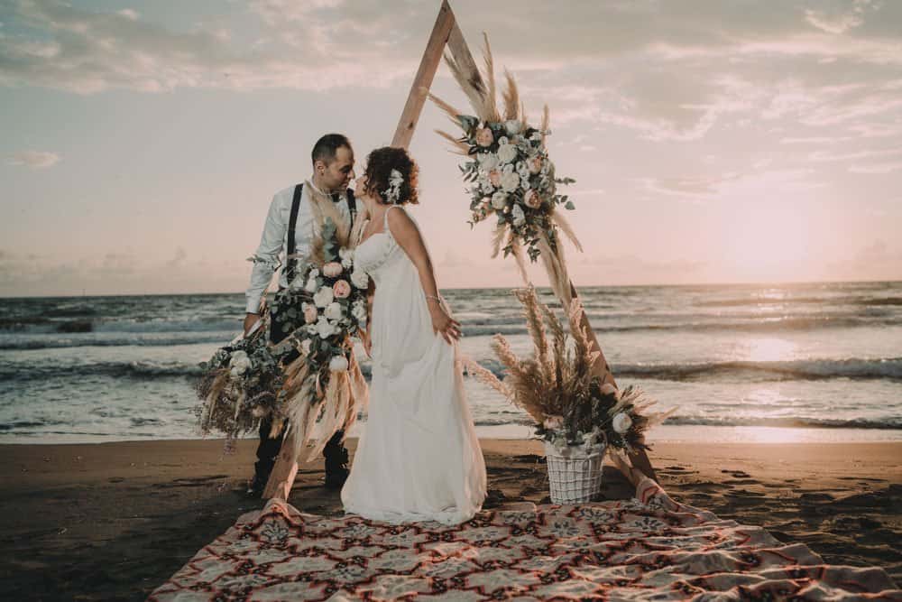 Elegant beach wedding ceremony with floral arch at sunset, showcasing high-end wedding venue and luxurious decor.