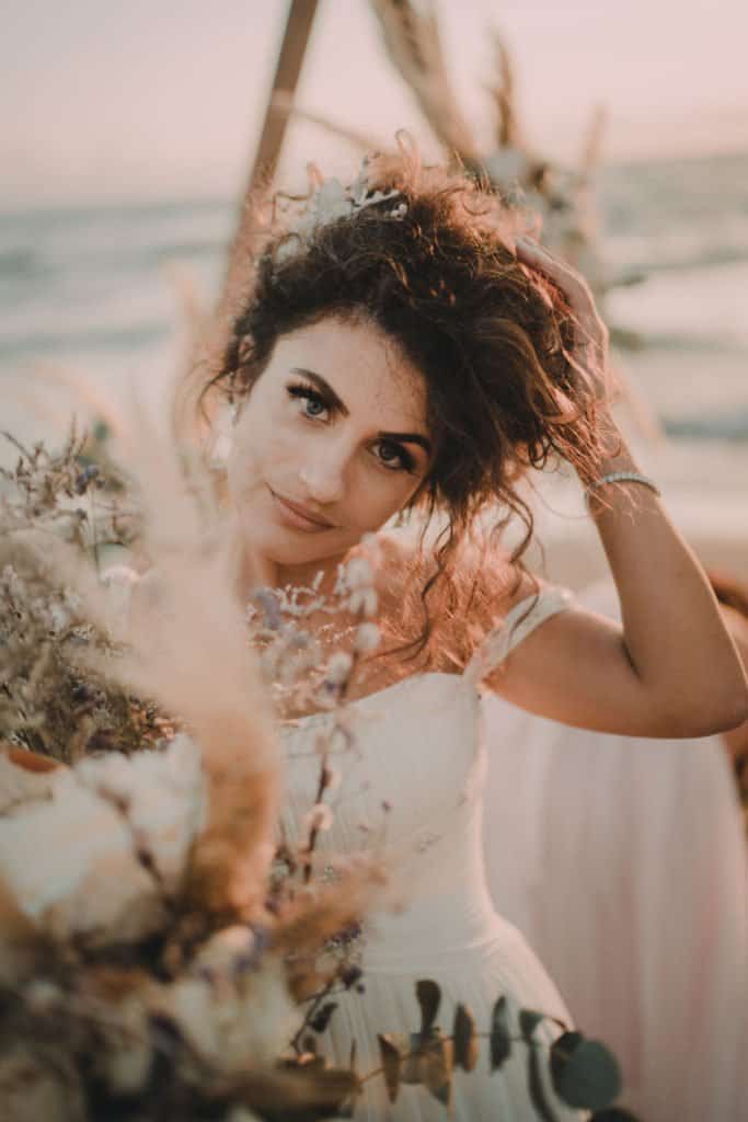 Elegant bride with curly hair at a luxury beach wedding, capturing high-end event details and scenic seaside backdrop.