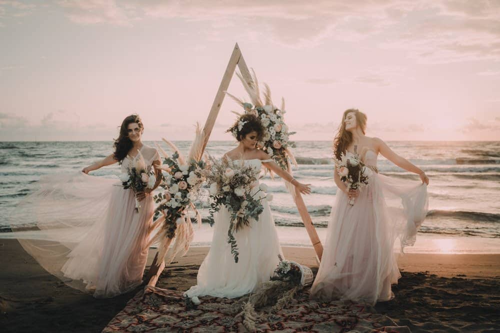 Elegant beach wedding with flowing bridesmaid dresses and floral arrangements at sunset.