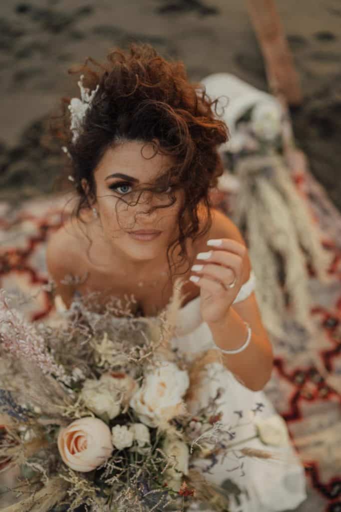 Elegant bride with curly hair holding a stunning bouquet at a luxurious outdoor wedding.