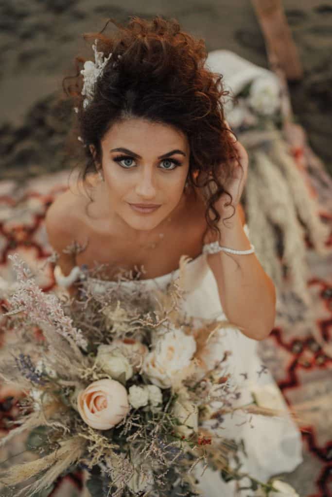 Elegant bride on a luxurious beach wedding, holding a stunning floral bouquet, with high-end venue details in the background.