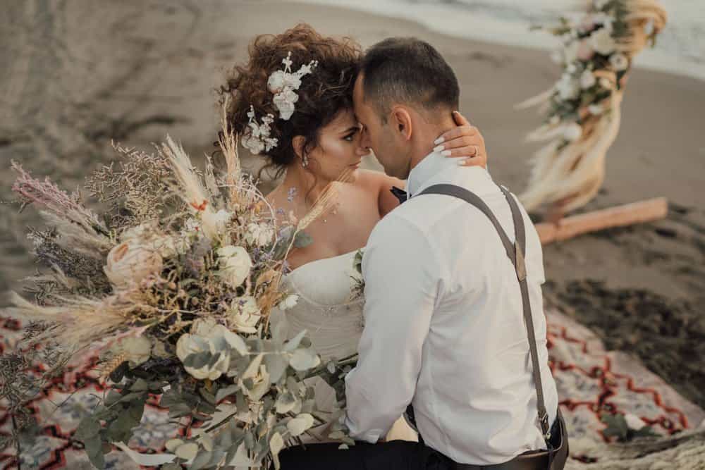 Elegant couple on a beach during a luxury wedding ceremony, with floral arrangements and decorative elements for high-end venues.