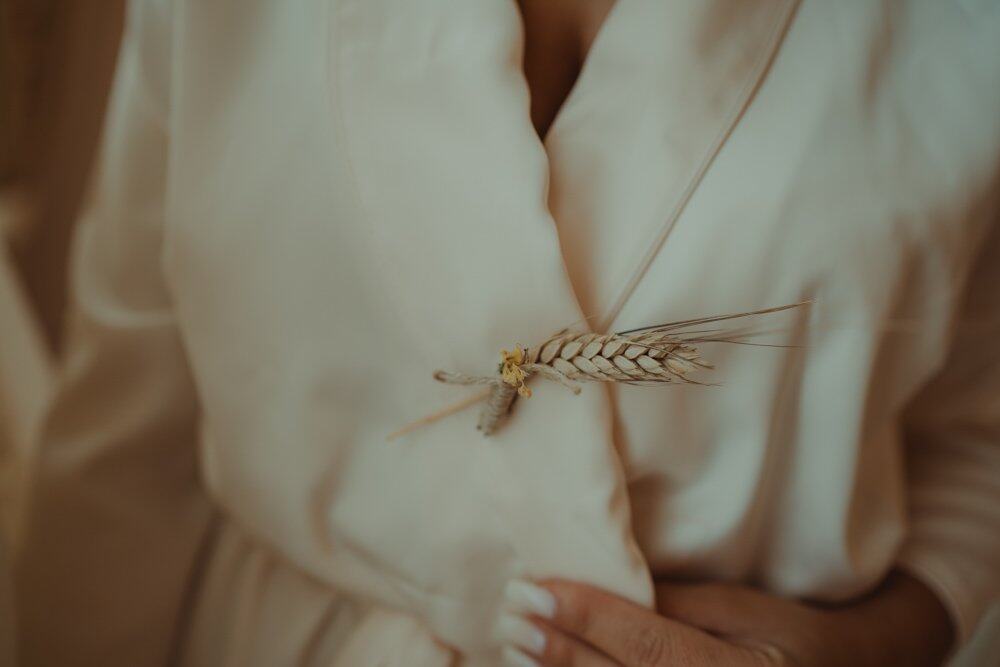 Golden wheat brooch pinned to an elegant silk wedding dress.