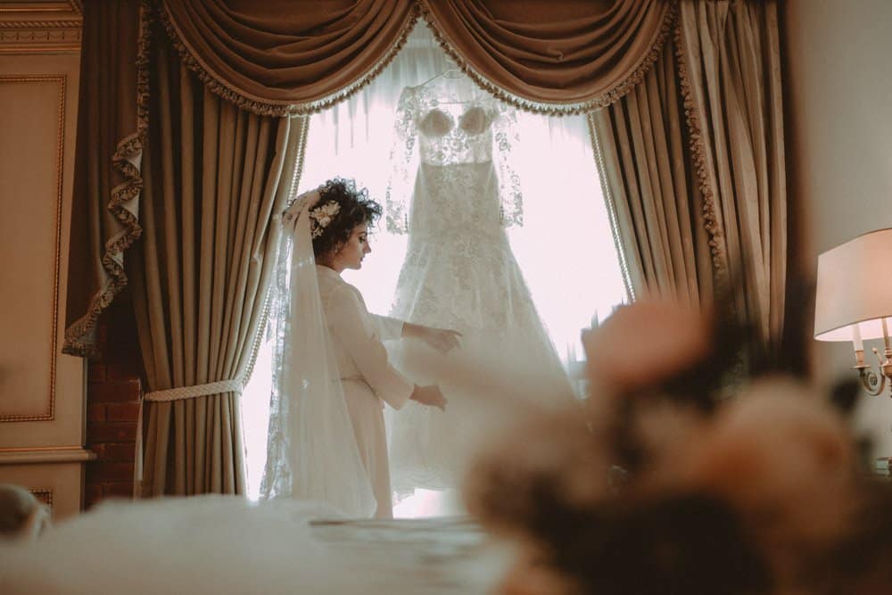 Elegant bride admiring a luxury wedding dress in a lavish high-end venue with opulent drapery and classic decor.