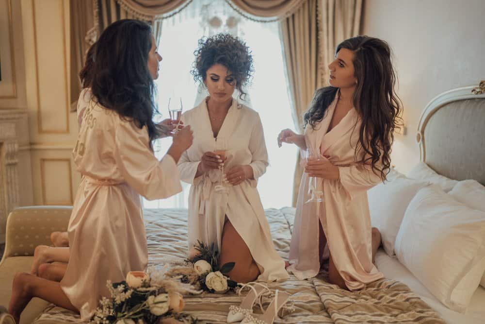 Elegant bridal party in satin robes enjoying pre-wedding celebration in luxurious hotel suite.