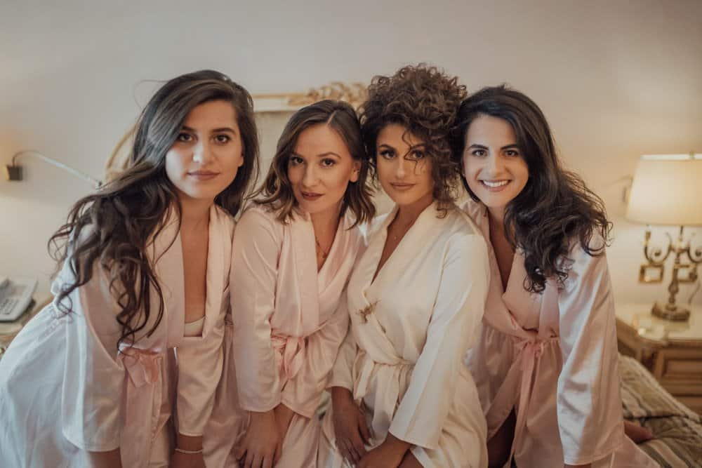 Bride squad in satin robes celebrating wedding day in elegant hotel room.