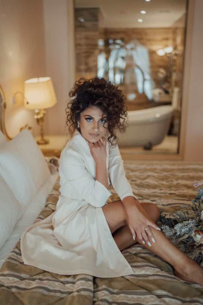 Luxury wedding bride in elegant white dress relaxing in upscale hotel room.
