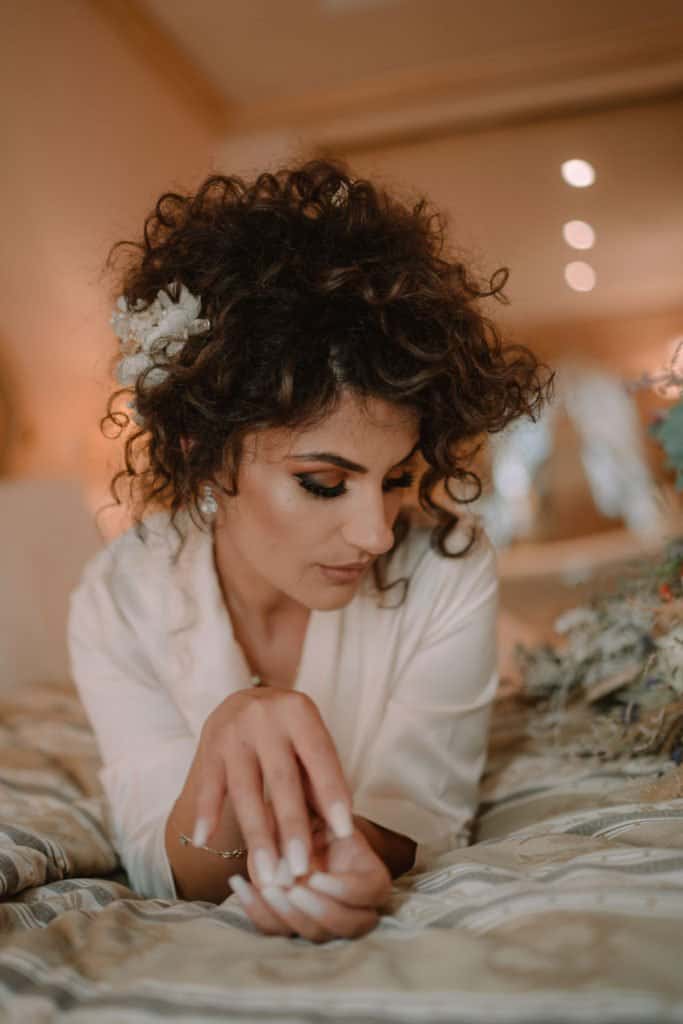 Luxury bride with curly hair and floral hairpiece in elegant bridal robe at wedding prep.
