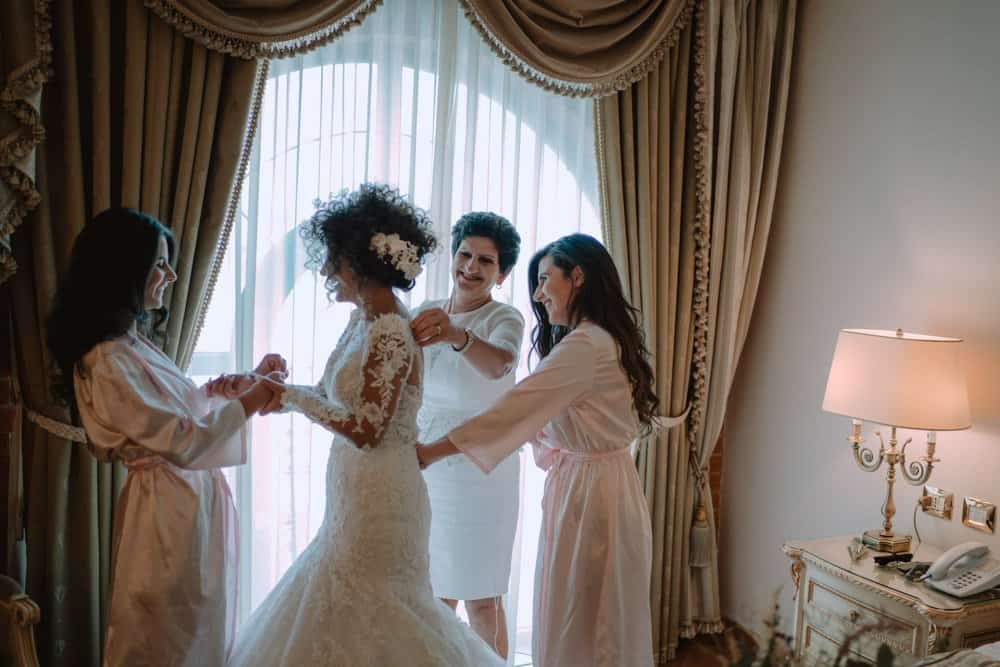 Elegant wedding preparations with bridesmaids helping bride in luxurious hotel room, high-end wedding venue, sophisticated decor and classic lighting.