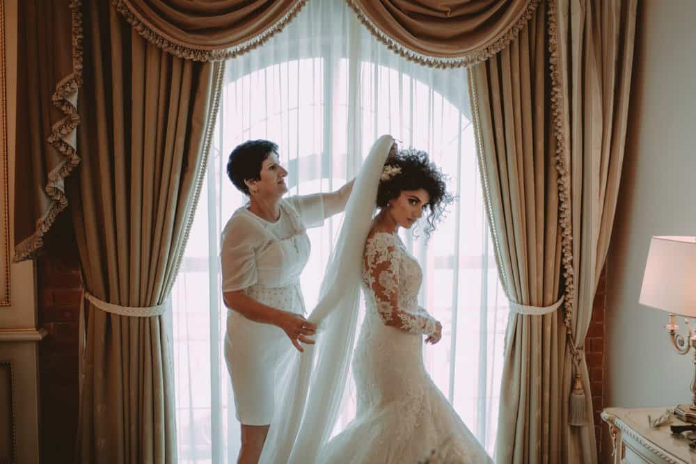 Elegant bridal gown fitting in a luxurious hotel suite with classic drapery and soft lighting.