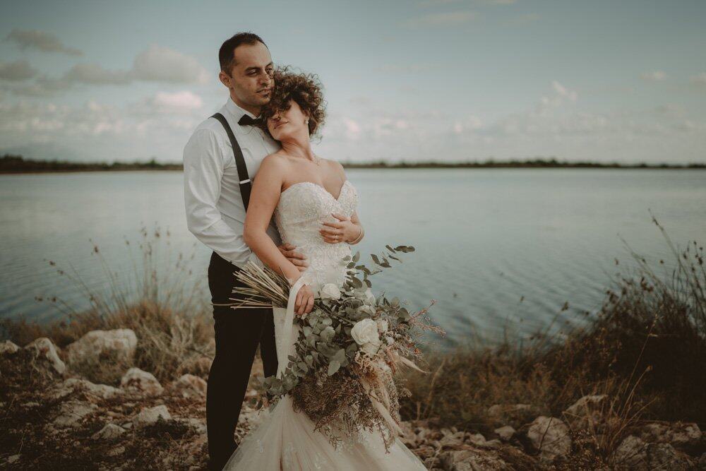 Elegant couple embracing by water at luxury outdoor wedding venue, romantic high-end wedding celebration.