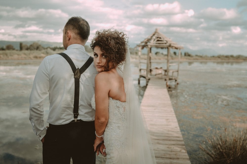 Elegant wedding couple by a serene lakeside pier at sunset, perfect for luxury wedding photography.