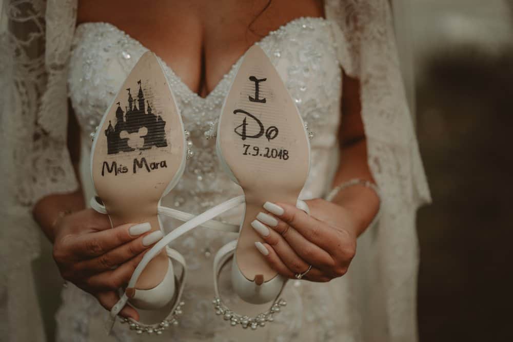 A woman in a wedding gown holding personalized wedding shoes with custom artwork and the wedding date.