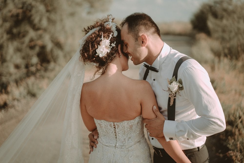 Romantic wedding couple in vintage attire embracing outdoors at sunset.