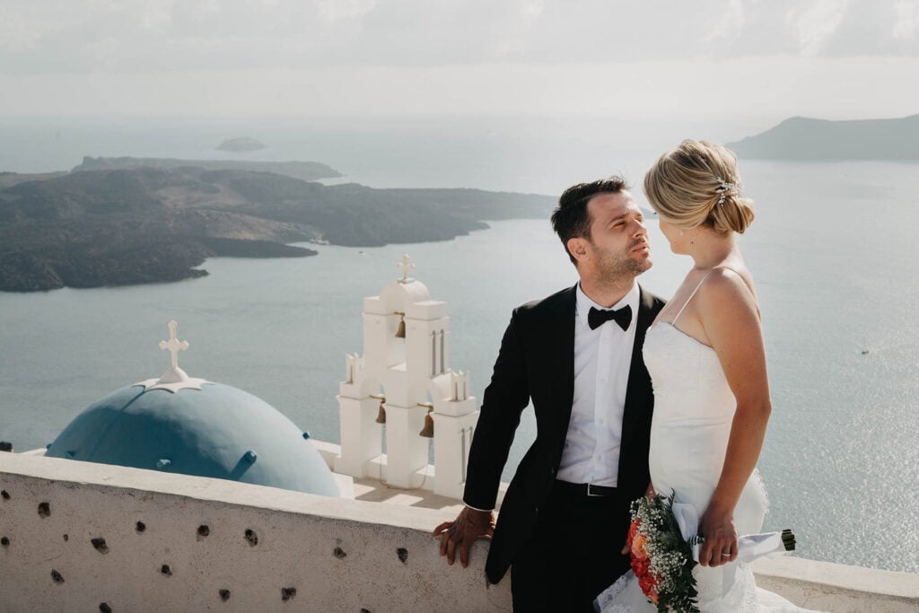 Elegant wedding couple on a cliffside overlooking the iconic Greek island landscape, perfect for luxury destination weddings.