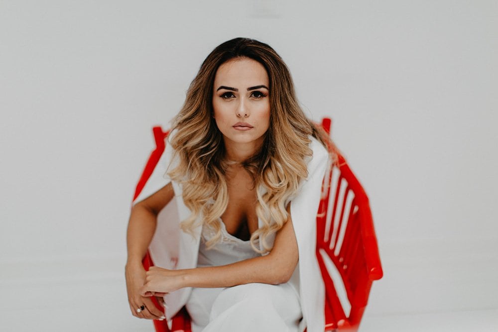 Glamorous woman with wavy hair sitting on a bold red chair, showcasing luxurious wedding fashion and high-end style.