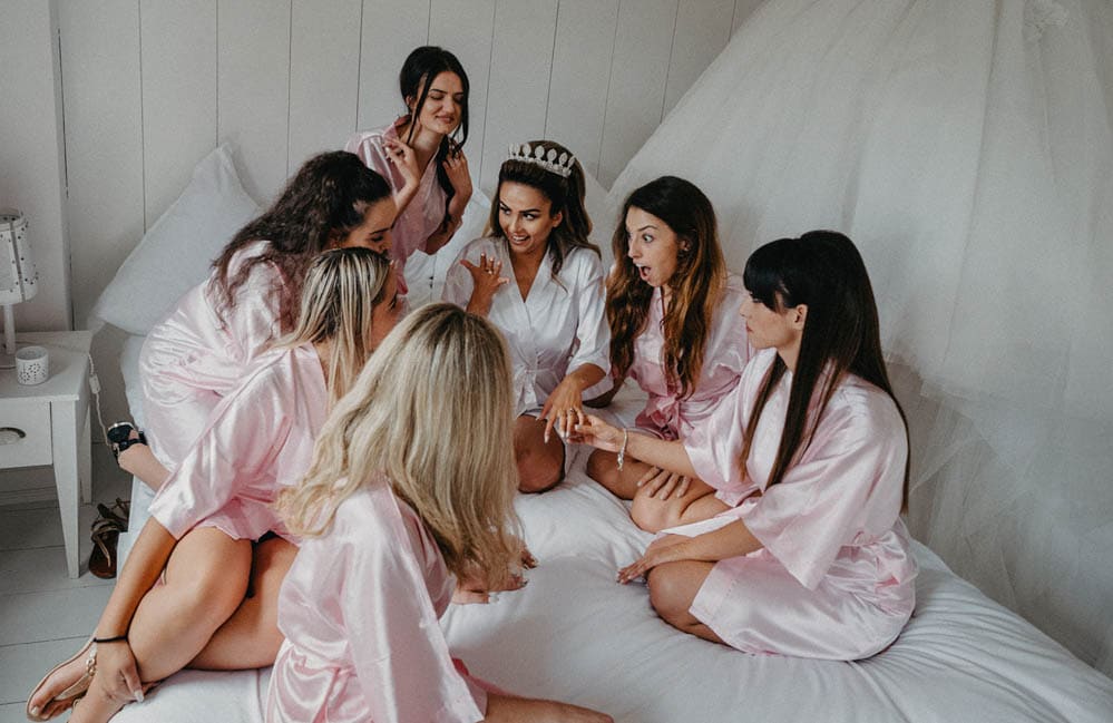 Bride and bridesmaids sharing moments before wedding in elegant pink robes, luxury wedding preparation, high-end bridal party, intimate wedding moments.