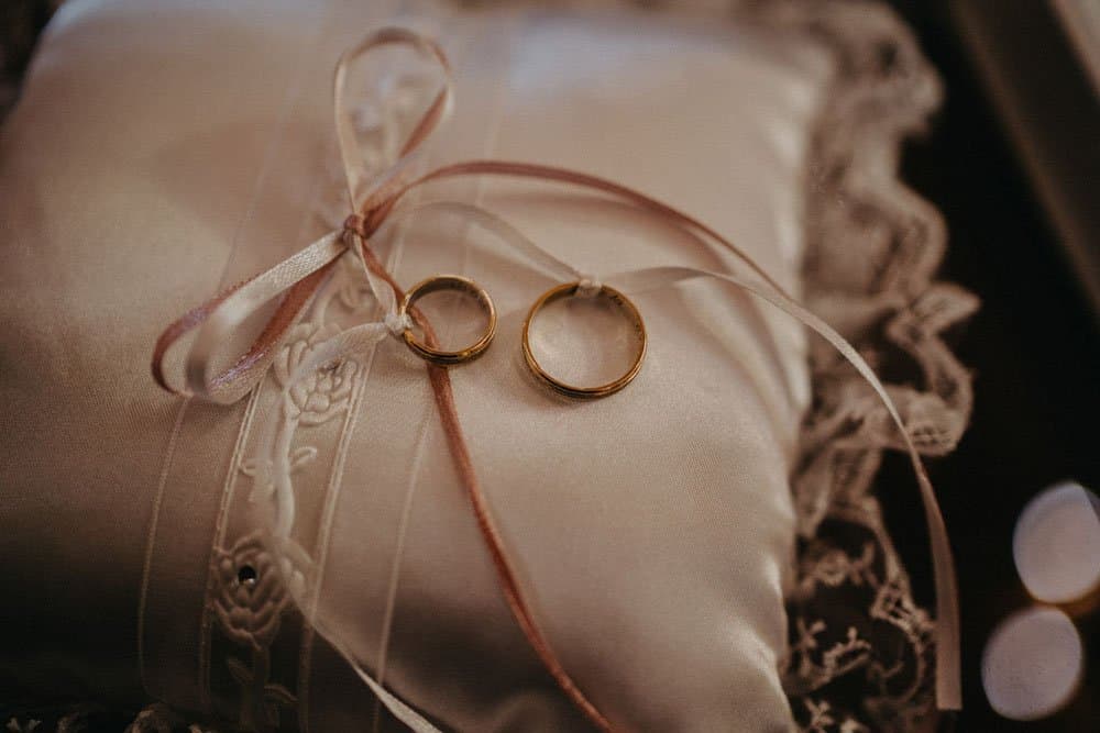 Gold wedding rings on satin pillow with lace detail.