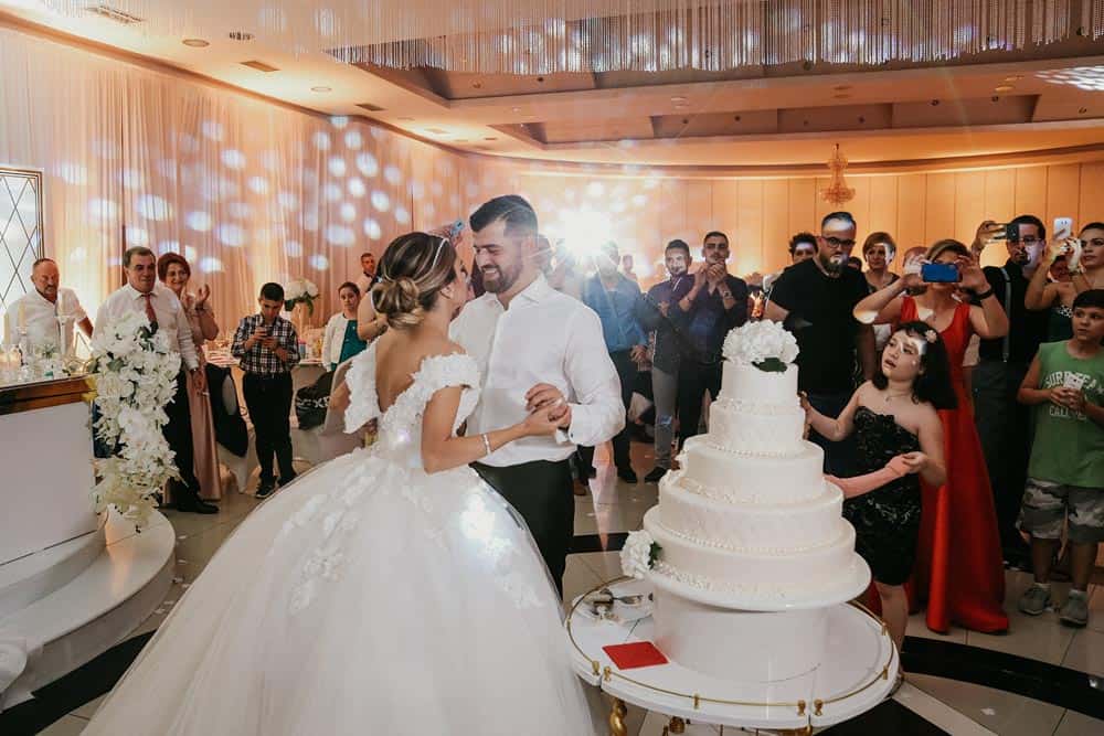 Elegant wedding reception at a luxury venue with a grand white wedding cake and joyful couple.