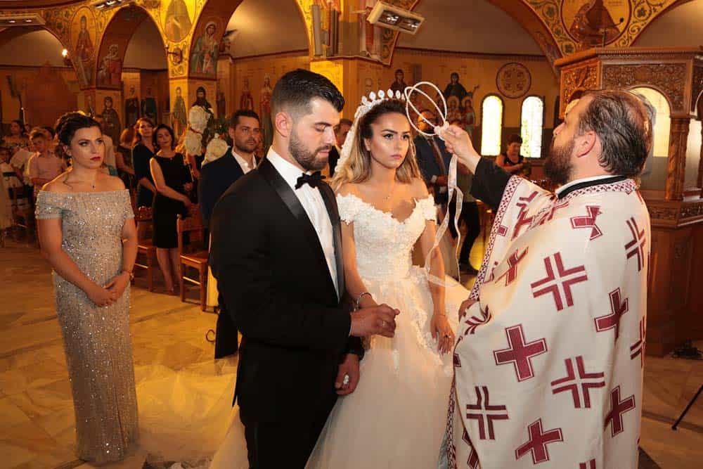 Elegant wedding ceremony with a priest blessing the couple inside a luxurious church setting. The bride and groom are dressed in exquisite attire, surrounded by family and friends.