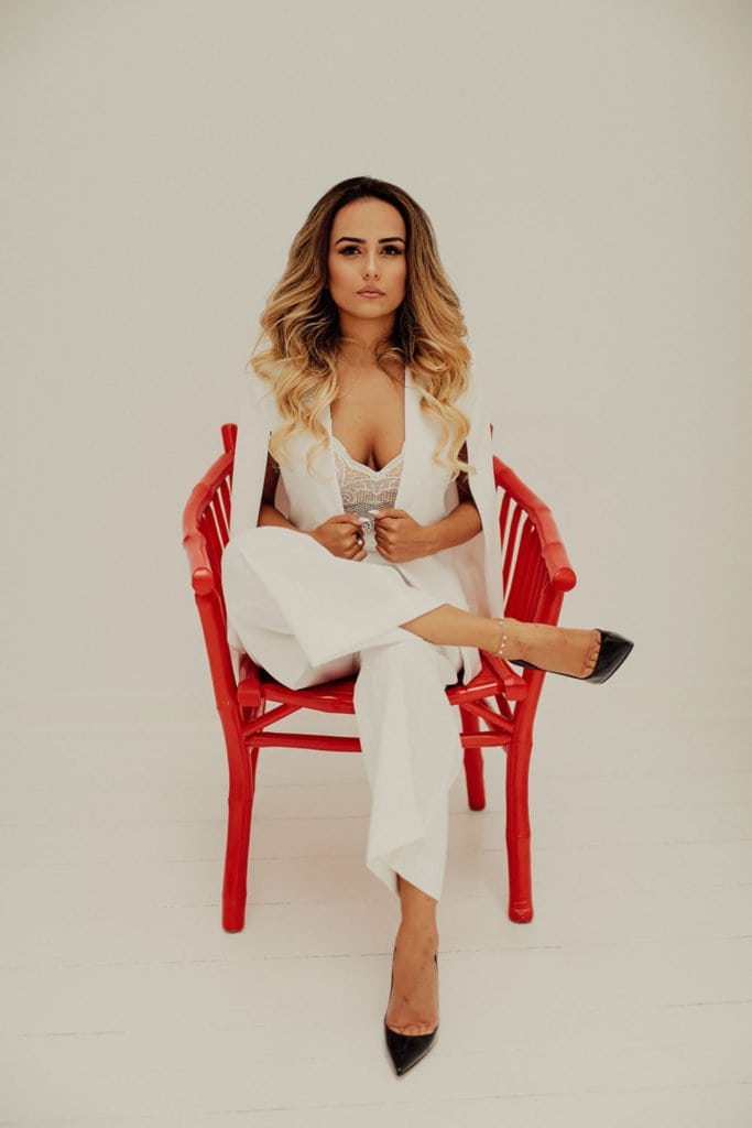 Elegant woman in white suit sitting on red chair, luxury wedding aesthetic, high-end venue styling, sophisticated bridal fashion.