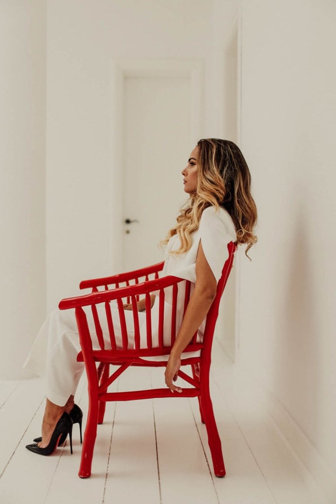 Elegant bride seated on a vibrant red chair in a luxurious wedding setting, showcasing high-end fashion and sophisticated decor.