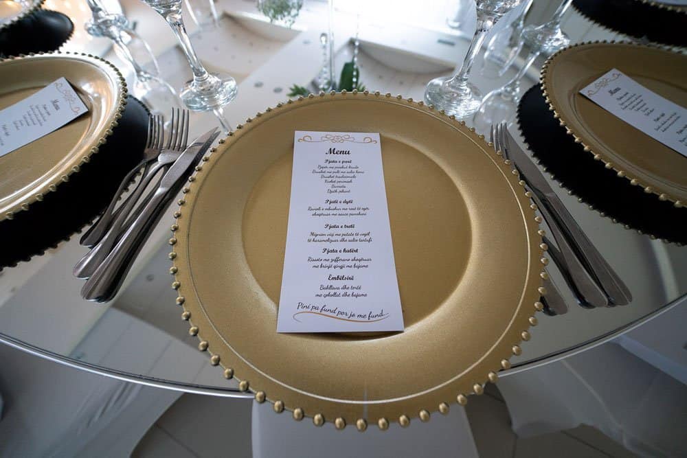Luxurious wedding table setting with elegant gold and black plates, crystal glasses, and personalized menu cards at a high-end venue.