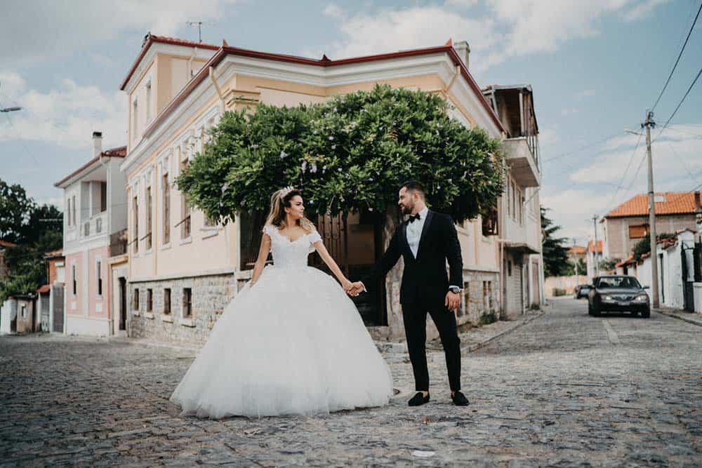 Elegant bride and groom holding hands outdoors in front of a charming vintage building, perfect for luxury wedding photos.