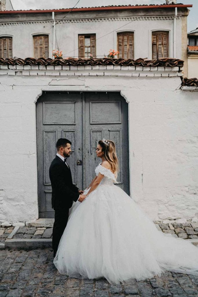 Elegant bride and groom holding hands outside a luxurious wedding venue with rustic gray doors.