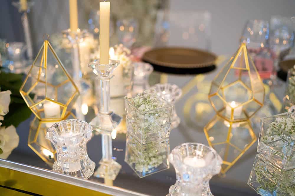 Elegant glass candles with floral accents and gold geometric decorations for a luxurious wedding table setting.
