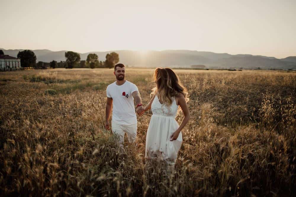 Golden hour romantic couple walking in a wheat field at sunset for luxury wedding photos.