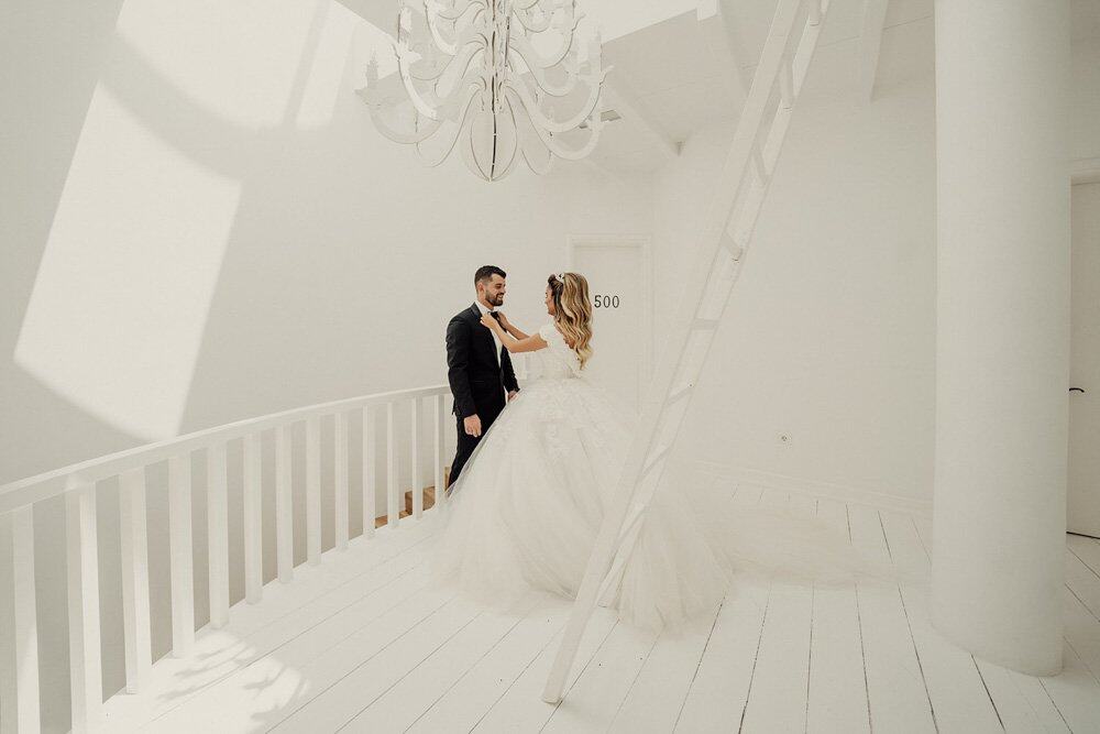 Elegant bride and groom in a luxurious white wedding venue with high ceilings and modern decor.
